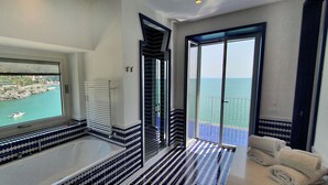 A modern bathroom with a bathtub, a glass shower enclosure, and a view of the sea. - In the blue painted blue (Campania)