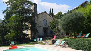 Une piscine dotée de chaises longues et d’un flotteur, entourée de verdure et bordée d’un bâtiment en pierre.