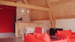 Un loft spacieux avec un plafond haut, un ensemble de canapés rouges, une table à manger et un coin cuisine.