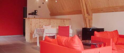 Un loft spacieux avec un plafond haut, un ensemble de canapés rouges, une table à manger et un coin cuisine.