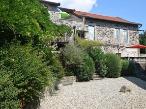 A stone building with a red-tiled roof, a balcony, and a gravel courtyard.