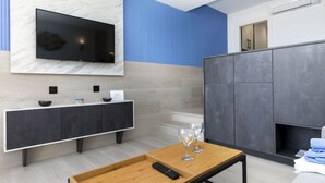 A modern living room with a flat-screen TV mounted on a marble wall, a dark grey cabinet, a wooden coffee table with a remote control, and two wine glasses. - Cosy apartment for 3 guests with WIFI, A/C, TV and balcony (Lloret De Mar)