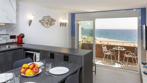 A modern kitchen with a view of the beach, a dining area with fruit and glasses, and a balcony with chairs and a table. - Cosy apartment for 3 guests with WIFI, A/C, TV and balcony (Lloret De Mar)