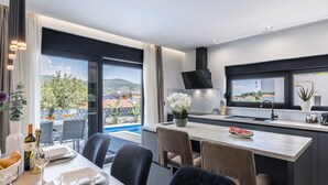 Eine moderne Küche mit großem Fenster, eine Essecke mit Tisch für zwei Personen und Blick auf einen Pool und Gebäude.