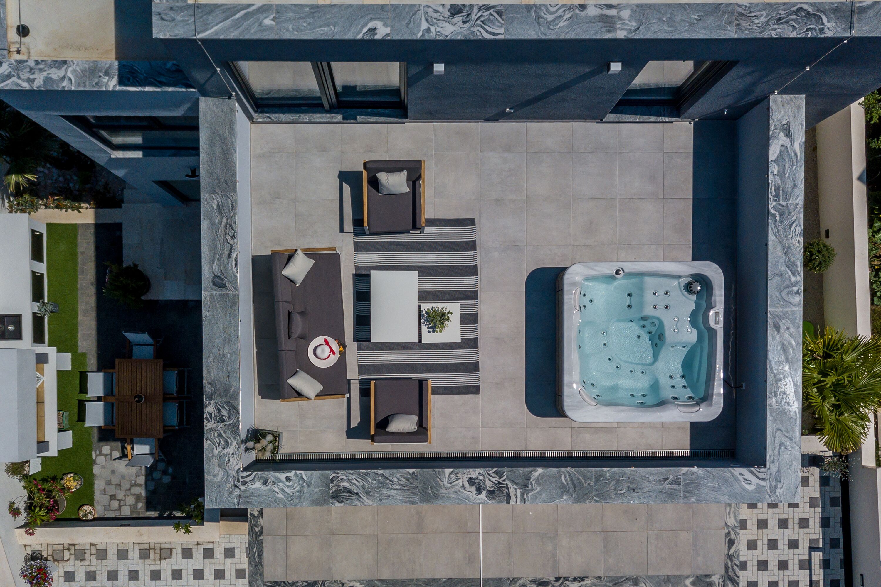 An aerial view of a rooftop patio with a hot tub, a dining area with a table and chairs, and a seating area with sofas and a rug.
