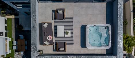 An aerial view of a rooftop patio with a hot tub, a dining area with a table and chairs, and a seating area with sofas and a rug.
