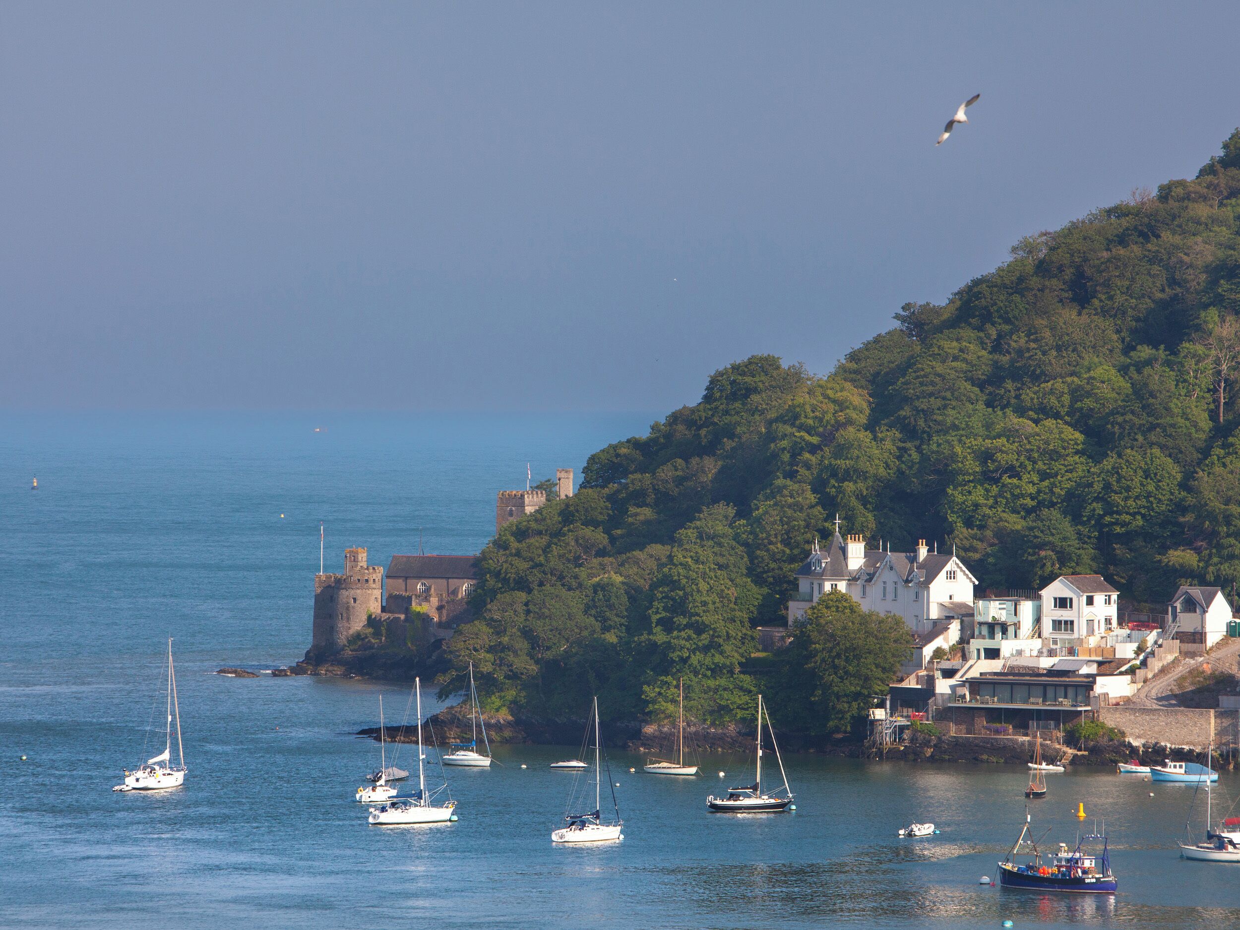 A coastal town with historic buildings, a castle, and various boats on the water.