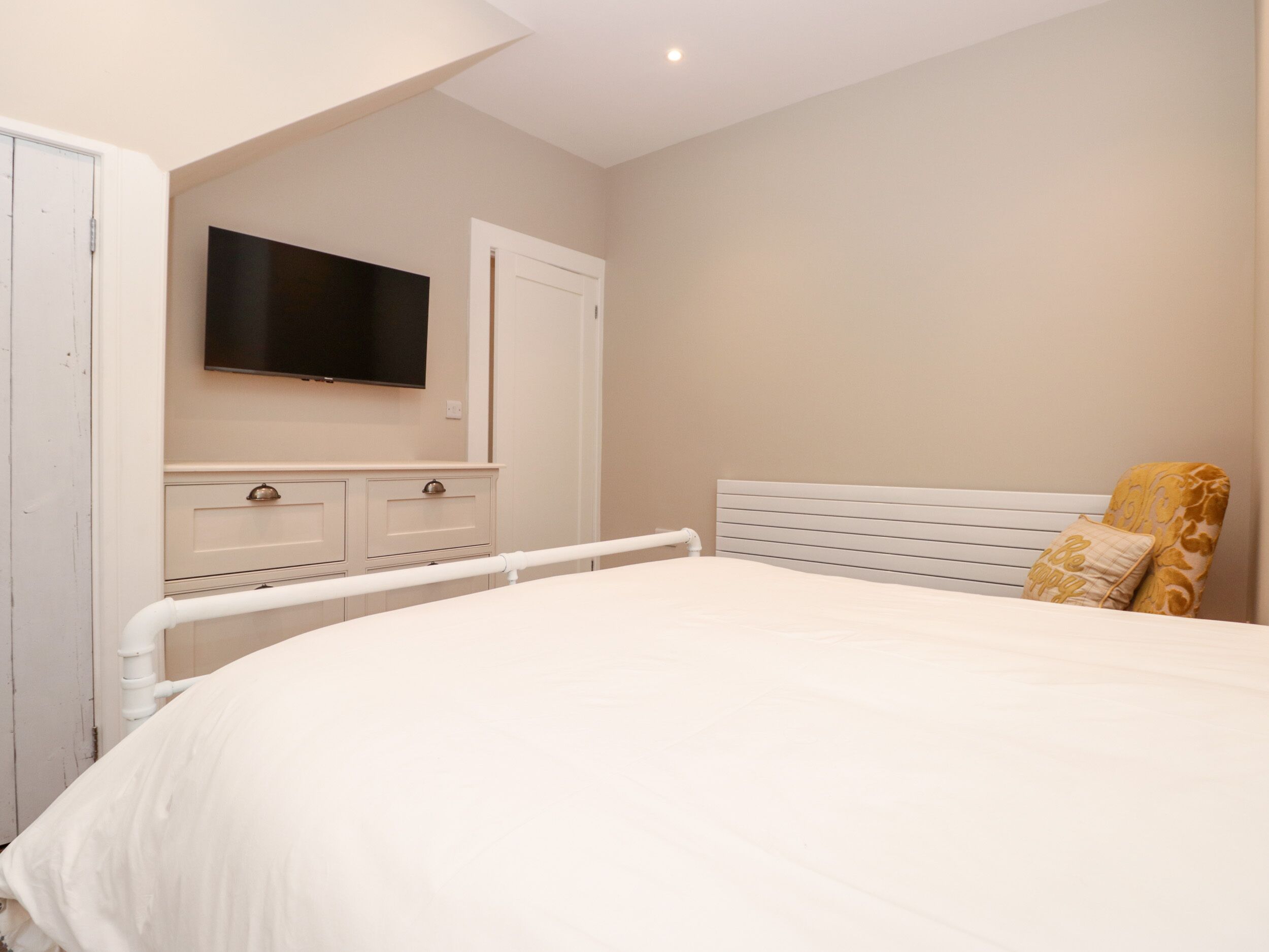 A bedroom with a bed, a TV mounted on the wall, a dresser, and a door.