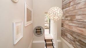 A hallway with framed artwork, a round mirror, a wooden wall, and a staircase leading to an outdoor area. - 44 Above Town (Dartmouth)