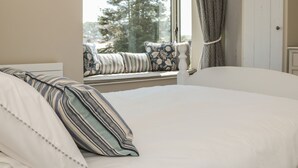 A bedroom with a large bed, a window with a view of trees, a curtain, and a bedside table. - 44 Above Town (Dartmouth)