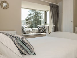 A bedroom with a large bed, a window with a view of trees, a curtain, and a bedside table.