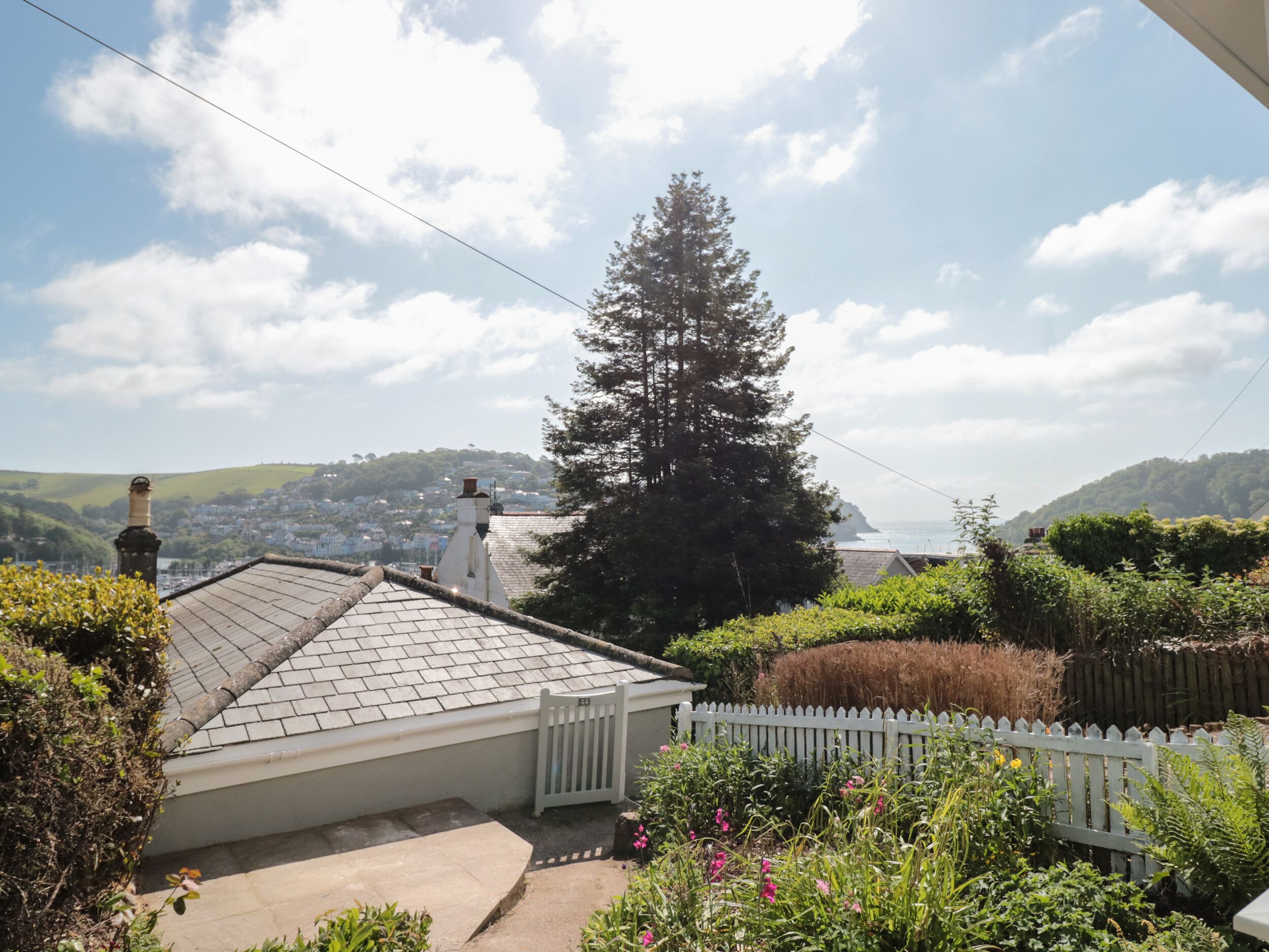 A residential area with a white picket fence, a large coniferous tree, and a view of a distant town.