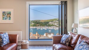 A living room with a large window overlooking a harbor, two leather sofas, a coffee table, and a framed painting on the wall. - 44 Above Town (Dartmouth)