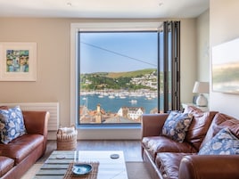 A living room with a large window overlooking a harbor, two leather sofas, a coffee table, and a framed painting on the wall.