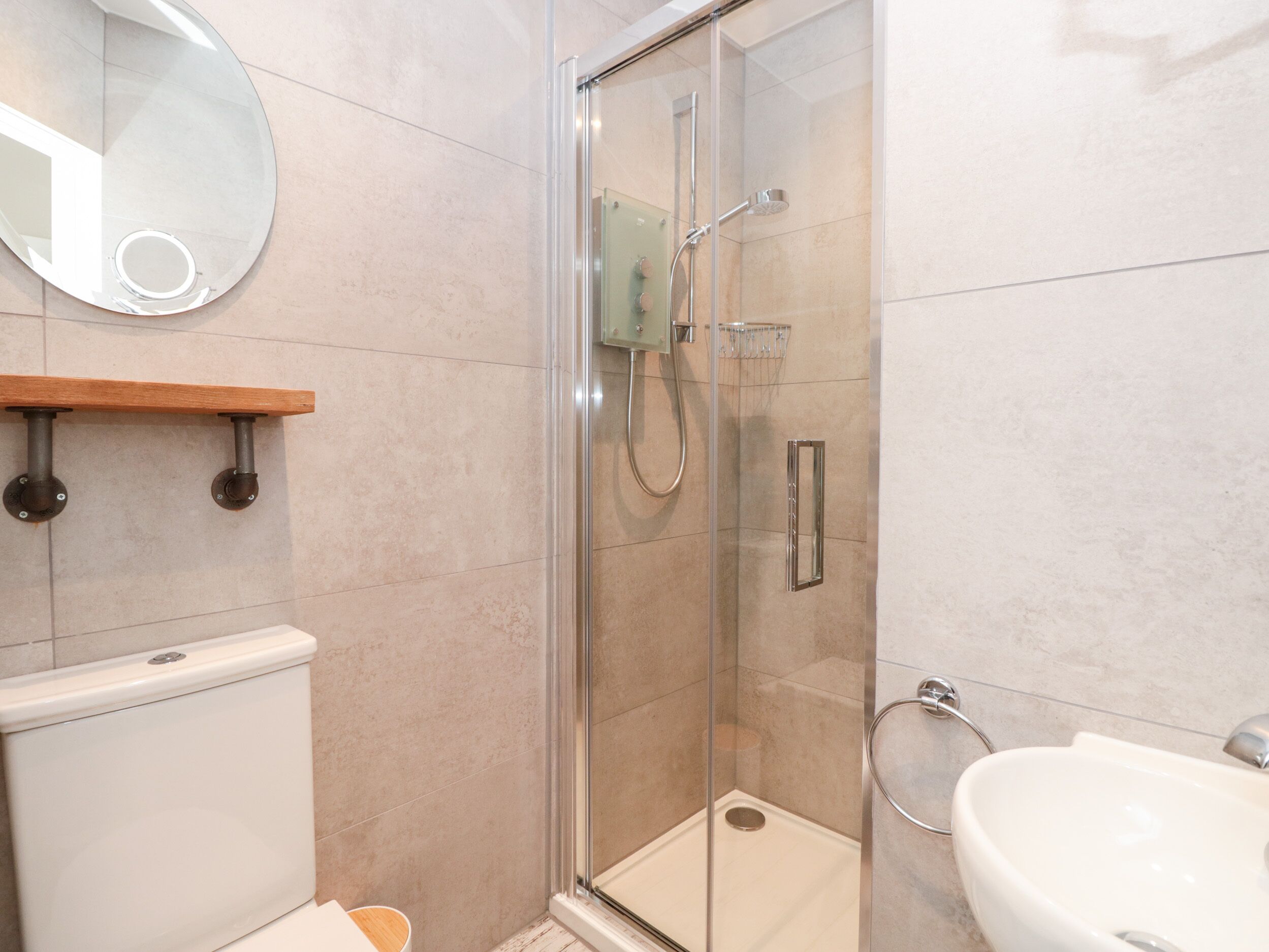 Une salle de bain moderne avec une douche à parois de verre, des toilettes, un lavabo et une étagère en bois.