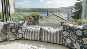A cozy seating area with patterned cushions, a view of a harbor with boats, and a glimpse of the surrounding landscape. - 44 Above Town (Dartmouth)
