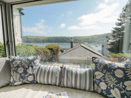 A cozy seating area with patterned cushions, a view of a harbor with boats, and a glimpse of the surrounding landscape.