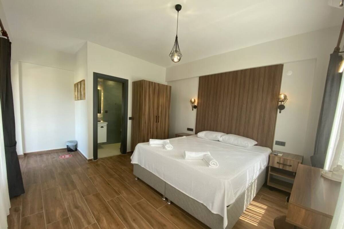 A hotel room with a large bed, wooden flooring, a wooden headboard, a bedside table, and a nightstand.