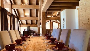 A wooden dining table set for a meal with red bowls and wine glasses, surrounded by cushioned chairs in a rustic interior with exposed wooden beams. - Holiday home in Saint-Martin-de-Belleville (Saint-Martin-de-Belleville)