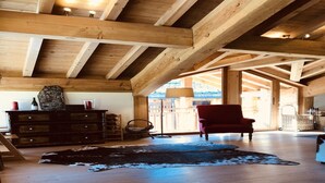 A spacious loft with exposed wooden beams, a leather rug, a red armchair, and a wooden dresser with decorative items. - Holiday home in Saint-Martin-de-Belleville (Saint-Martin-de-Belleville)