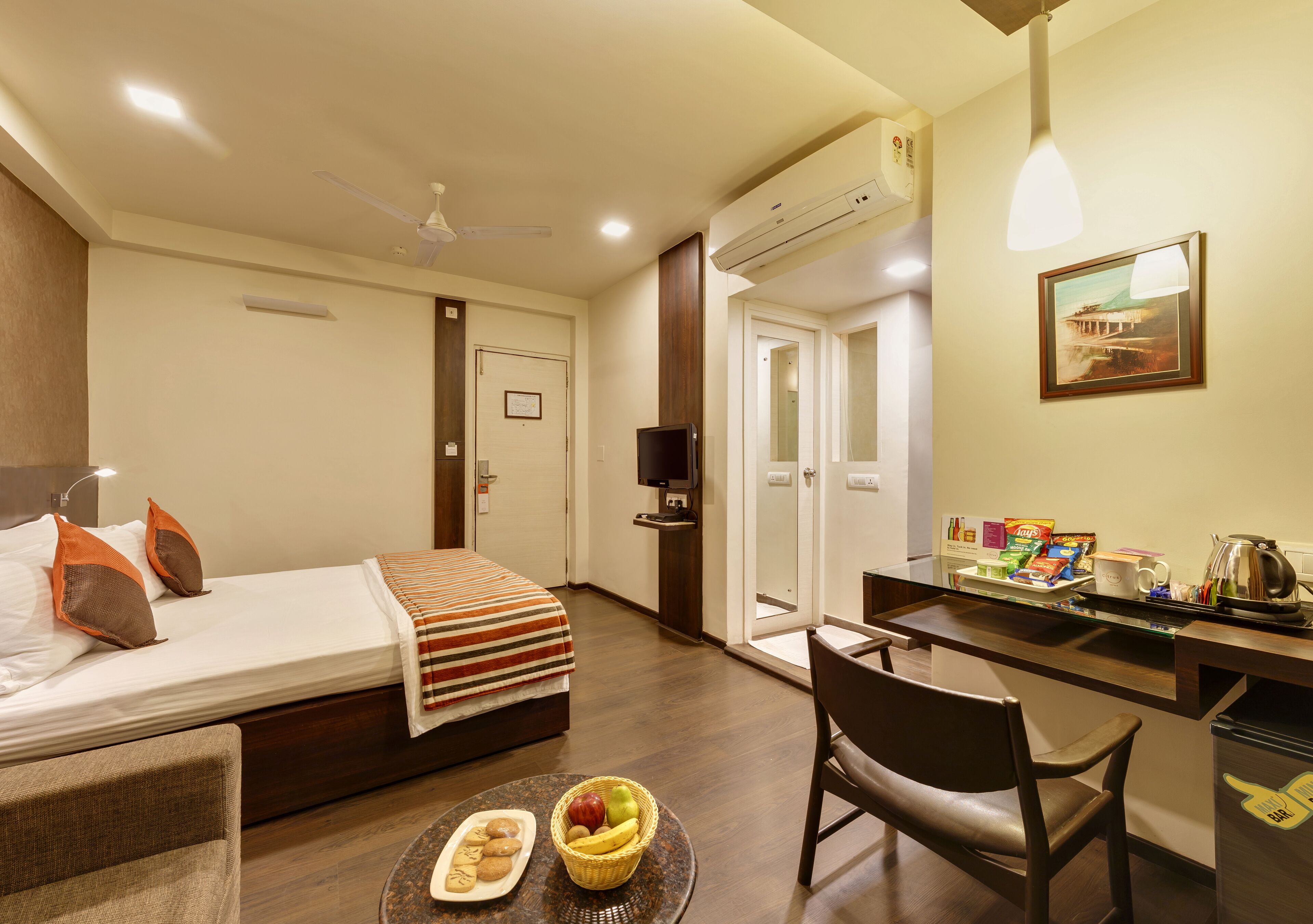 A hotel room with a bed, a desk, a chair, a dining table with food, and a TV.