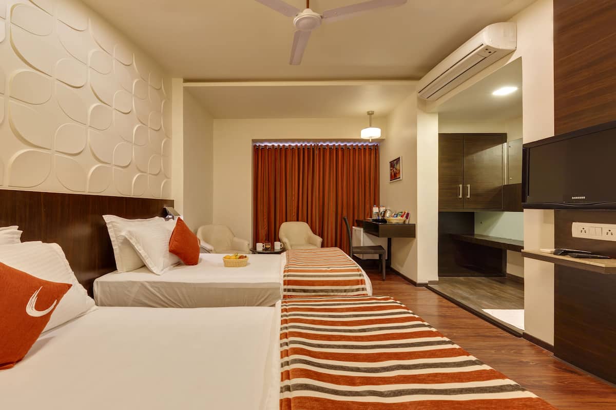 A hotel room with two beds, a desk, a television, and an air conditioning unit.