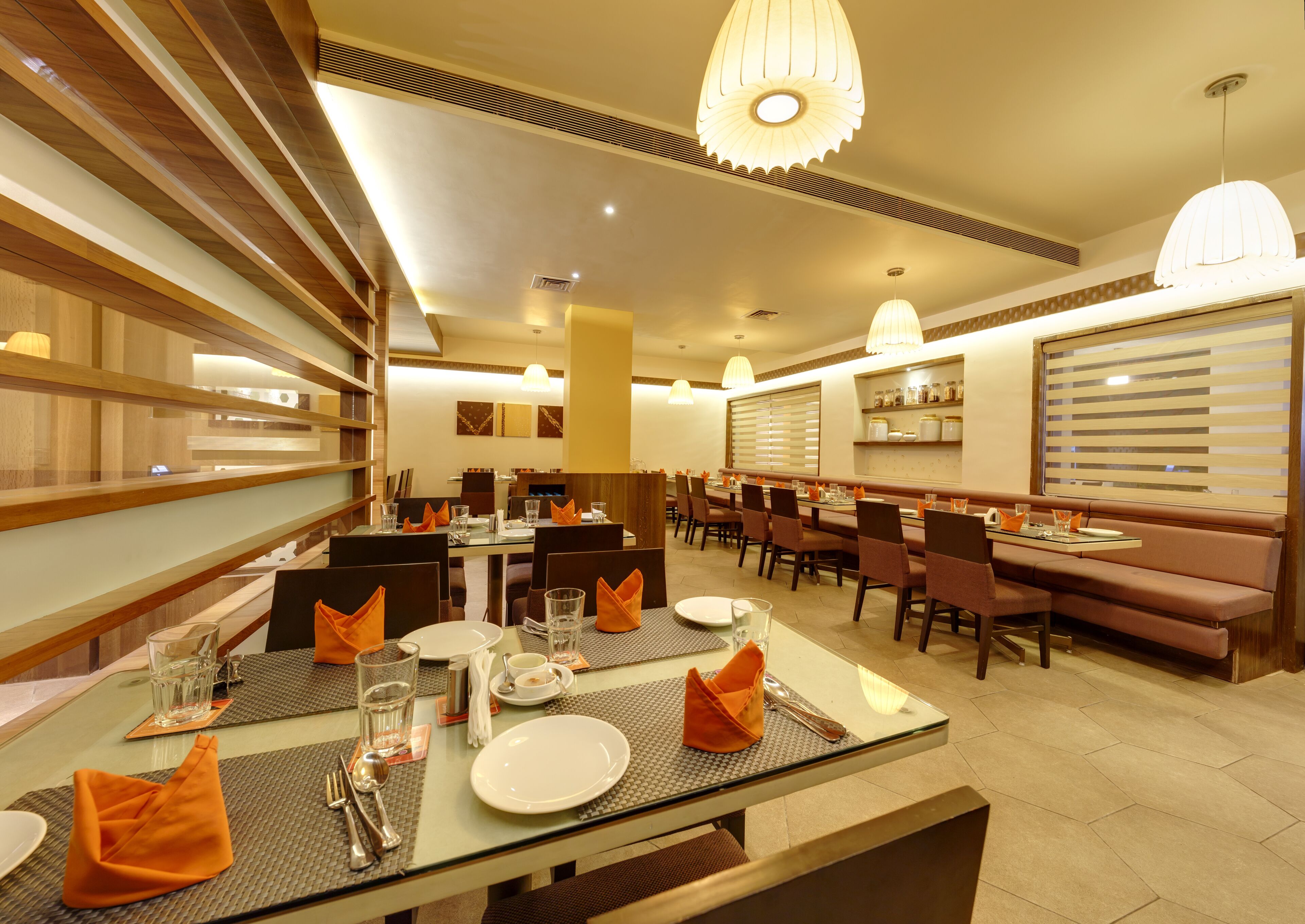 A restaurant with a long communal table, individual booths, and a high ceiling with pendant lighting.