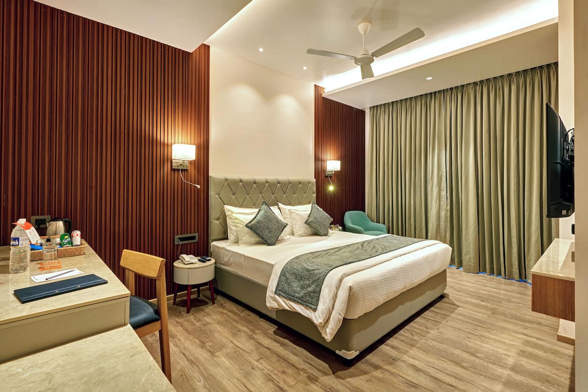 A hotel room with a bed, bedside table, lamp, and a desk with a chair.