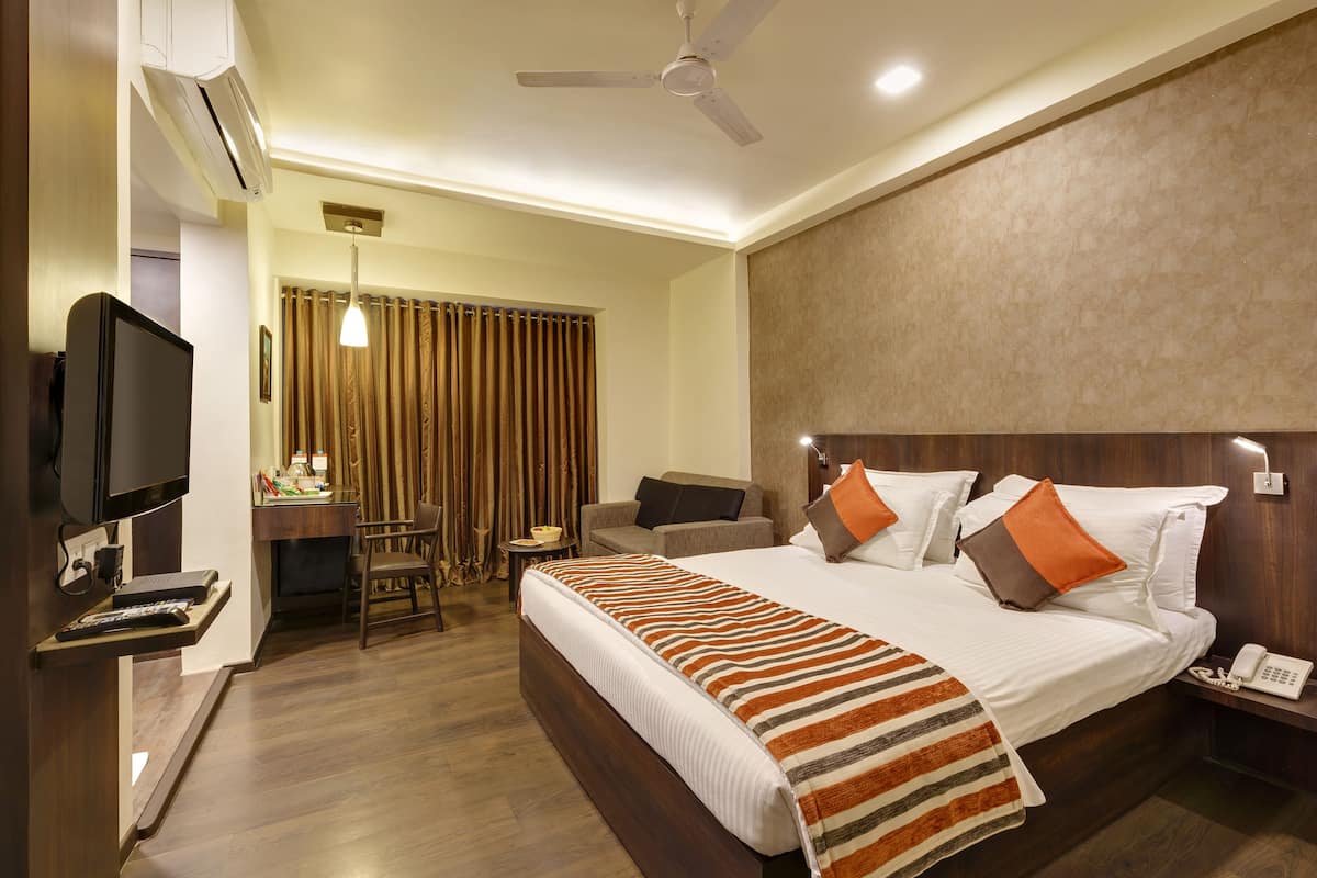 A hotel room with a bed, a desk, a chair, a television, and a ceiling fan.