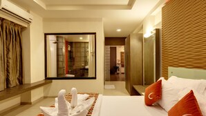 A hotel room with a bed, a bathroom visible through a glass door, and a wooden headboard. - Regenta Place Raysons Kolhapur  (Kolhapur)