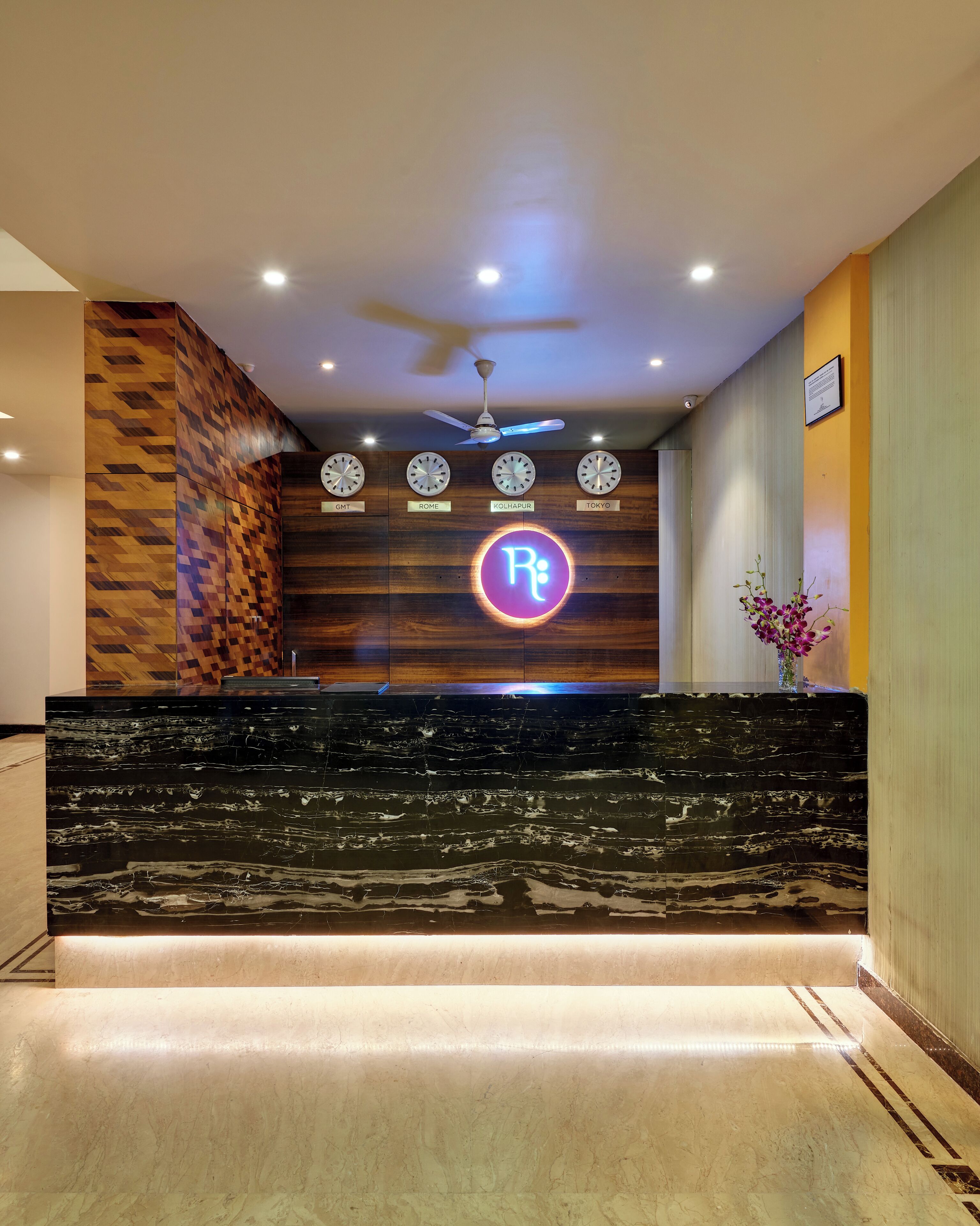 A reception area with a modern design, featuring a marble counter, a ceiling fan, and clocks indicating GMT, Rome, Kolkata, and Tokyo times.
