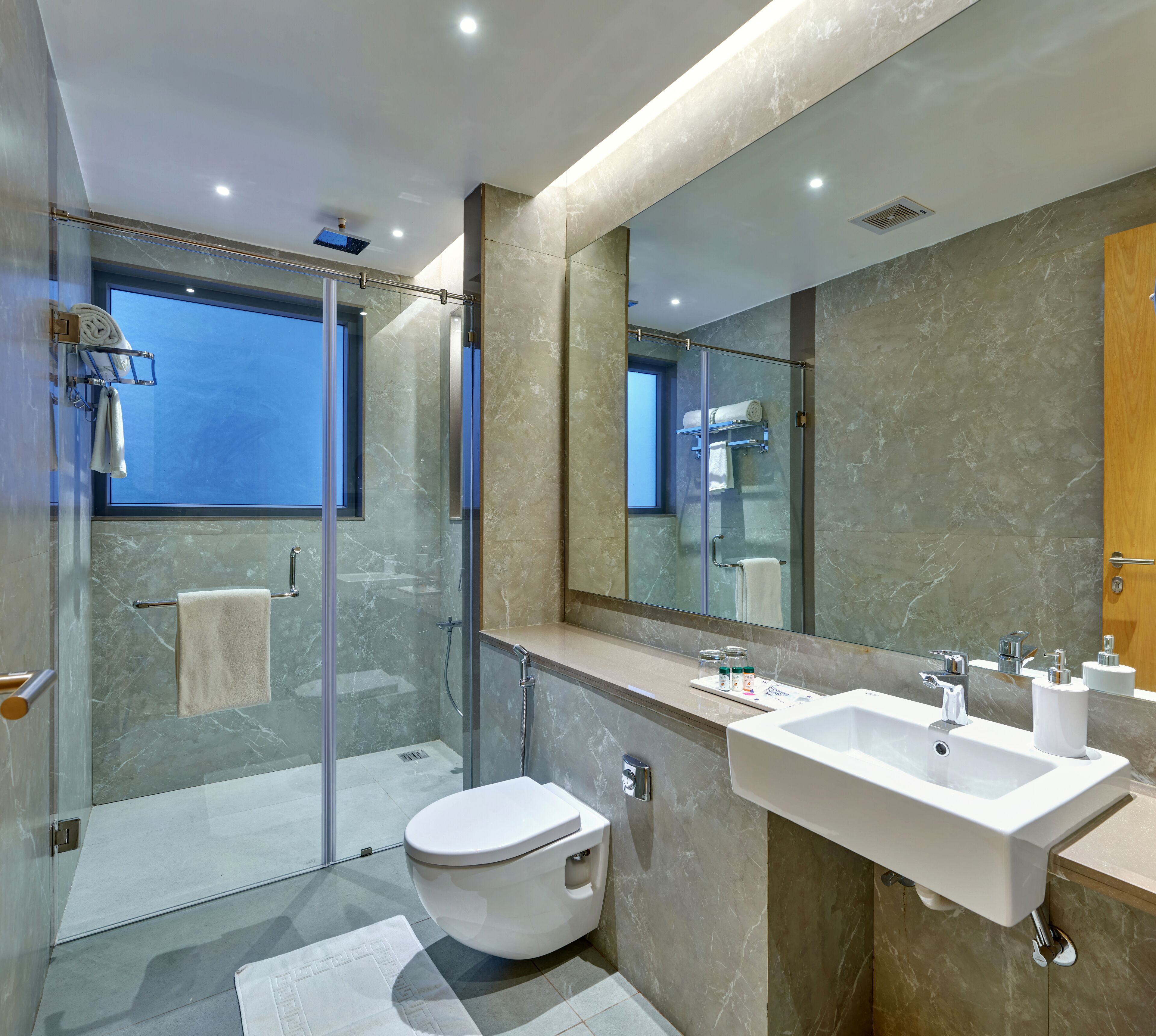 Un baño moderno con ducha envuelta en vidrio, inodoro blanco y un lavamanos espacioso con espejo.