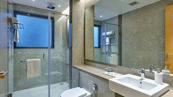Un baño moderno con ducha envuelta en vidrio, inodoro blanco y un lavamanos espacioso con espejo.