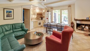 A living room with a green sofa, a red armchair, and a coffee table. There is a dining area with a table and chairs. The kitchen is visible in the background with cabinets and appliances. - Villa in Provence near Vaison-la-Romaine (Vaison-La-Romaine)