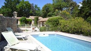 A swimming pool with lounge chairs, a stone wall, and a garden with trees and shrubs. - Villa in Provence near Vaison-la-Romaine (Vaison-La-Romaine)