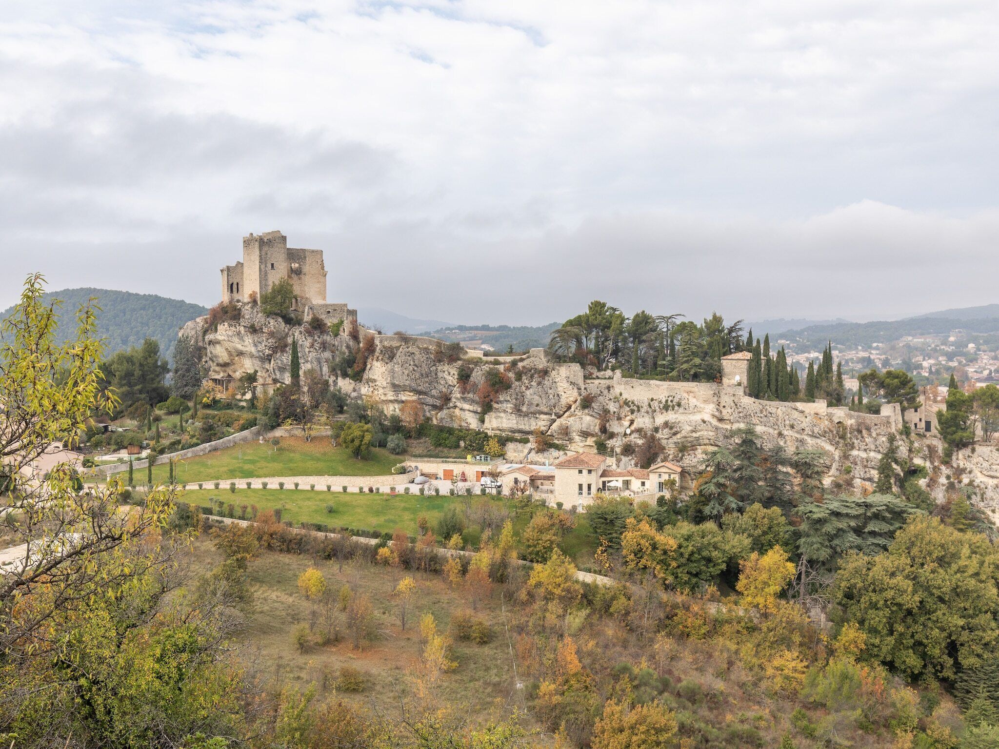 Un château historique perché sur une colline rocheuse, surplombant une ville, et entouré d’arbres et de verdure.