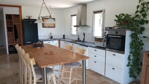 Une cuisine moderne avec des meubles blancs, une table à manger en bois et une plante suspendue.