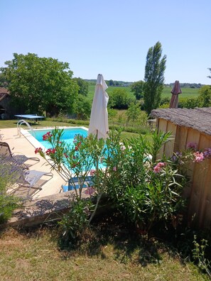 A swimming pool with a sun umbrella, lounge chairs, and a wooden shed in a garden. - Maison Neuve Avec Piscine Privée (Meyrals)