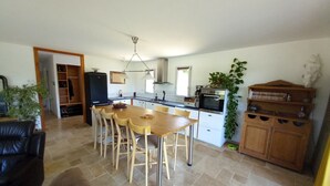 Un salon spacieux avec une table et des chaises de salle à manger en bois, un canapé en cuir noir et un coin cuisine doté de meubles blancs et d’un four encastré.