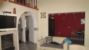 A living room with a sofa, a television, and a fireplace. There is a red door and a staircase in the background. - Chalet near the beach in Messinia (Messinia)