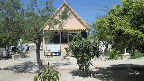 A small, single-story building with a tiled roof and a covered seating area with a table and chairs. - Chalet near the beach in Messinia (Messinia)