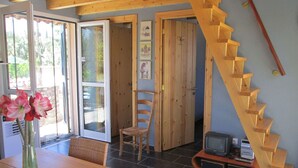A room with a wooden staircase, a dining table with chairs, a vase of flowers, and a television on a wooden stand. - Chalet near the beach in Messinia (Messinia)