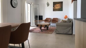 Un salon moderne comprenant un coin repas, un canapé, deux fauteuils, une table basse, un téléviseur et un tableau accroché au mur.