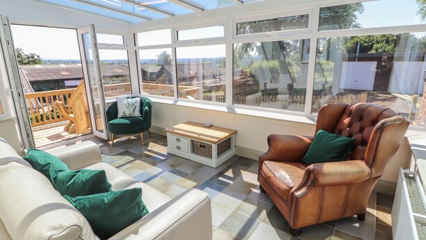 Un solárium con vistas al campo, un sillón de cuero, un sofá blanco y un sillón verde.