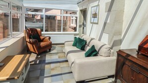 Un solárium con techo de vidrio, un sillón de cuero marrón, un sofá beige y un mueble de madera.