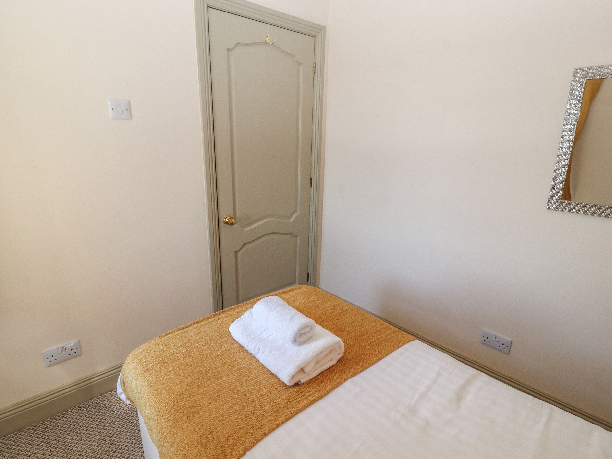 Une chambre d’hôtel avec un lit, une porte, un miroir et une prise électrique.
