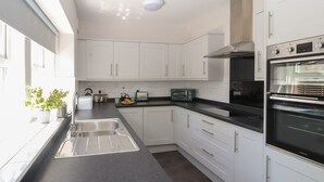 Una cocina moderna con armarios blancos, encimera negra y electrodomésticos de acero inoxidable, incluyendo un microondas y un horno.