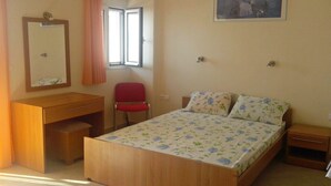 A bedroom with a wooden bed, a desk, a chair, a window with curtains, and a wall-mounted picture. - Apartment in Ravdoucha with Sea Views (Voukolies)