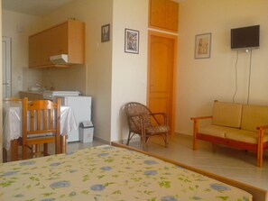 A small, cozy room with a bed, a sofa, a chair, a kitchen area with a refrigerator, and a television mounted on the wall. - Apartment in Ravdoucha with Sea Views (Voukolies)