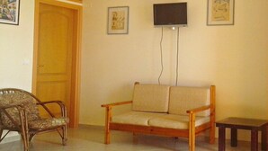 A living room with a wooden chair, a sofa, a small table, and a TV mounted on the wall. - Apartment in Ravdoucha with Sea Views (Voukolies)